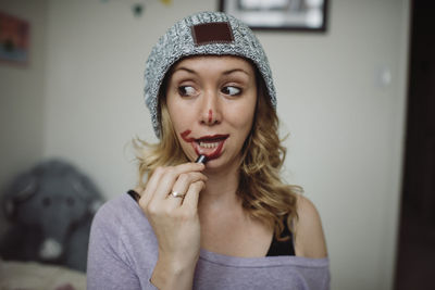 Playful woman applying lipstick while standing at home