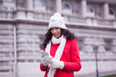 Young woman using phone while standing in city during winter