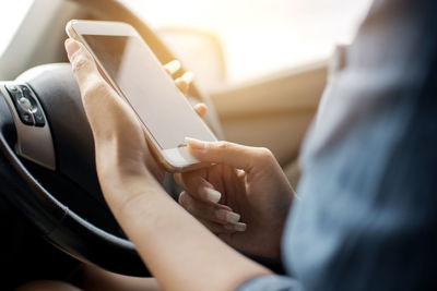 Cropped hands of woman using mobile phone in car