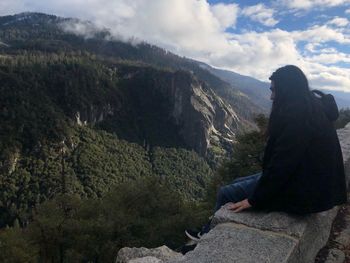 Man sitting on mountain against sky