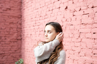 Young woman looking away while standing against stone wall