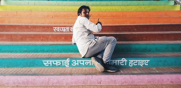 Full length of man using mobile phone sitting on staircase