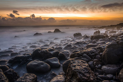 Rocks on shore against sky during sunset