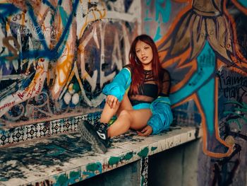 Portrait of smiling woman sitting against graffiti wall
