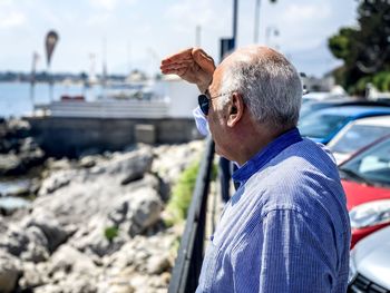 Side view of senior man shielding eyes while standing at beach