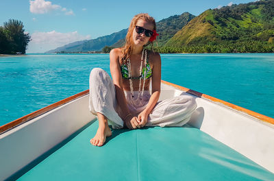 Portrait of woman wearing sunglasses while sitting in boat on sea against mountains and sky