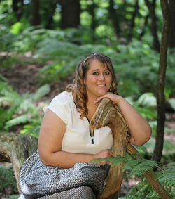 Portrait of overweight young woman sitting on log in forest