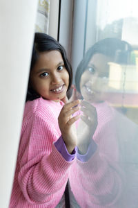 A cute indian girl child standing at the glass window looking at camera with reflection