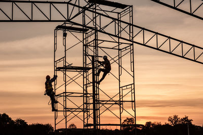 Low angle view of crane at construction site against sky during sunset