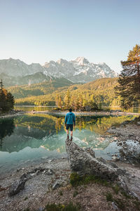 Rear view of man standing at lakeshore against clear sky