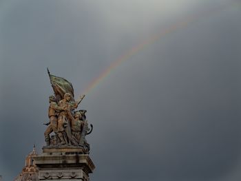 Low angle view of statue against rainbowed sky