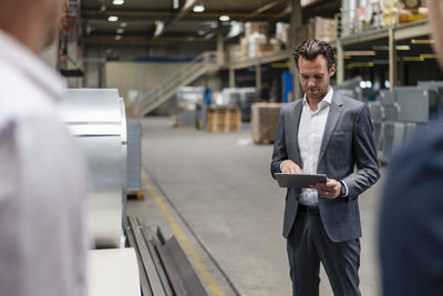 Businessman using digital tablet while standing near colleagues in factory