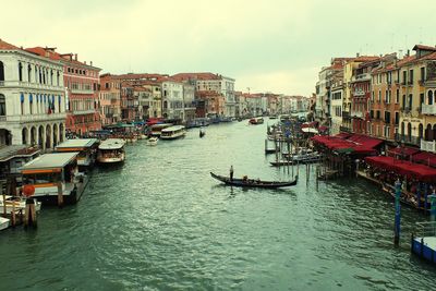 Boats in canal amidst city against sky