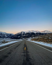 Road amidst snowcapped mountains against clear sky