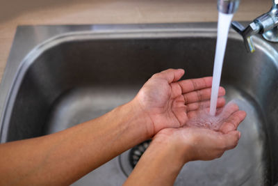Cropped image of hand touching water from faucet in bathroom