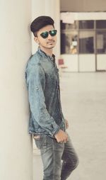 Portrait of young man wearing sunglasses standing against wall