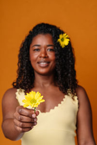 Portrait of young woman holding yellow flower against orange background