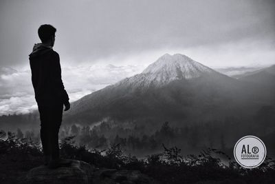 Rear view of man standing by mountain against sky