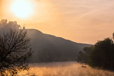 Man on small boat fishing at early morning foggy lake or river in golden colors