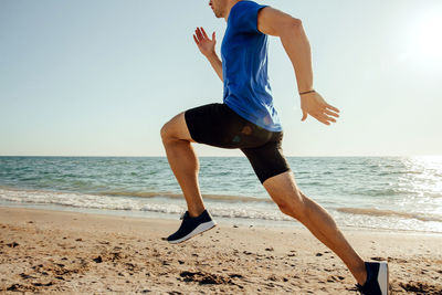 Low section of man running on shore at beach