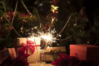 Close-up of lit sparklers by christmas presents at night