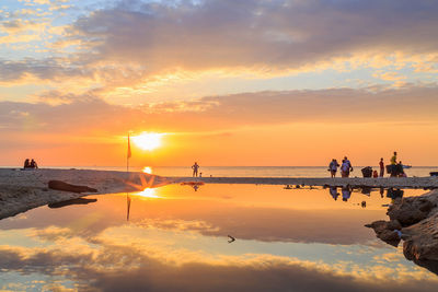 People on beach against sky during sunset