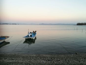 Boat moored in lake against sky during sunset