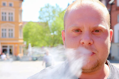 Close-up portrait of man exhaling smoke in city