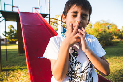 Cute boy gesturing while sitting on slide with eyes closed at playground