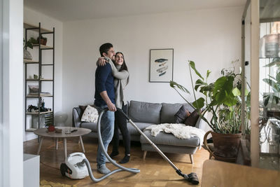 Happy couple embracing while cleaning living room at home