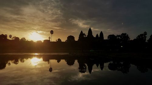 Silhouette trees by lake against sky during sunset