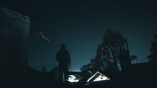 Rear view of silhouette man standing against sky at night