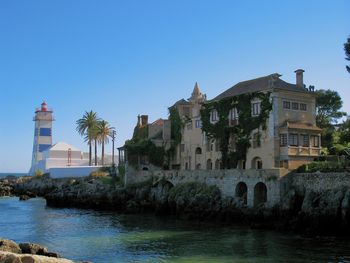 Buildings by river against clear blue sky