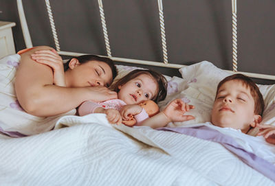 Mother sleeping with son and daughter on bed at home