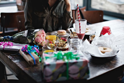 Midsection of young woman sitting with birthday presents and food on restaurant