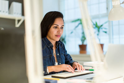 Confident businesswoman using laptop while sitting at desk in creative office