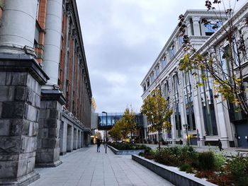 Empty road amidst buildings in city against sky