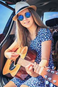 Portrait of smiling young woman playing guitar in car 