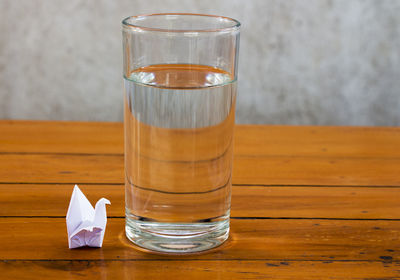 Paper crane by drinking water glass on wooden table