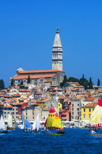 Sailboats in city by buildings against clear blue sky