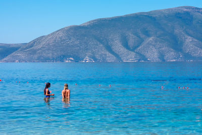 People swimming in sea against mountain