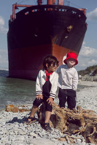 Two fashionable baby boys stand next to a large rio ship that ran aground off novorossiysk