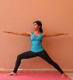 Full length of woman performing yoga while standing against orange wall