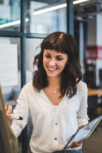Smiling businesswoman holding digital tablet while writing on whiteboard in office