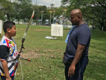 Side view of father standing with son practicing archery at park
