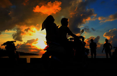 Silhouette people with motor scooter on pier against cloudy sky during sunset