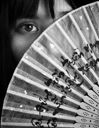Close-up portrait of woman hiding face behind folding fan