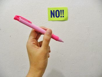 Cropped hand holding pen by adhesive note with no text on wall