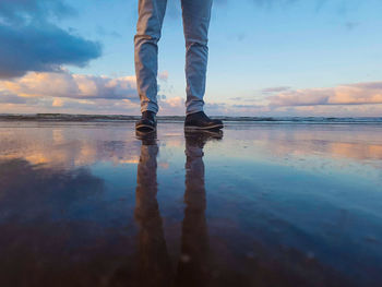 Low section of person standing on beach against sky during sunset