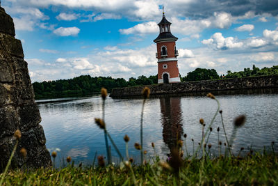 Tower by lake and buildings against sky